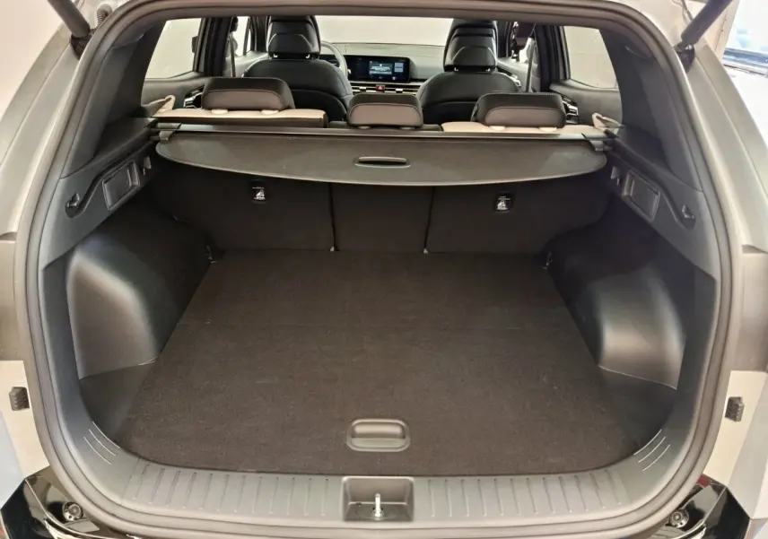 Coffre ouvert du KIA Sportage gris clair, vue arrière montrant l’espace de chargement et la plage arrière rétractable.