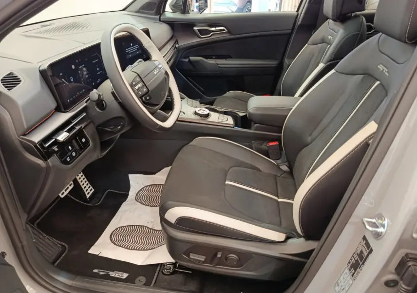 Intérieur avant droit du Kia Sportage gris clair 2026, sièges GT-Line noirs avec surpiqûres blanches et tableau de bord numérique.