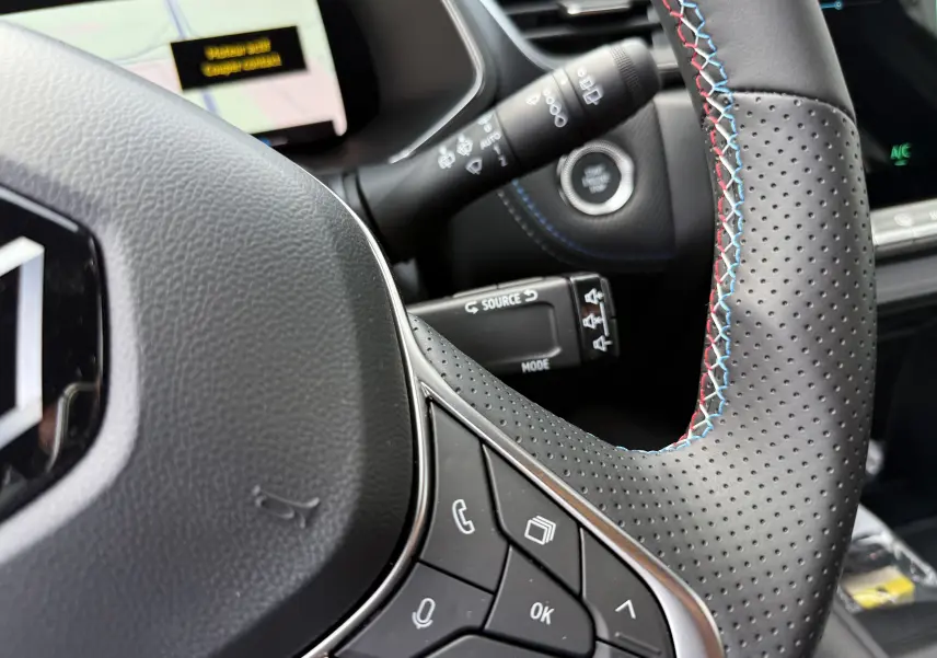 Gros plan sur le volant perforé avec surpiqûres tricolores du Renault Captur hybride 2025, boutons de commande visibles.