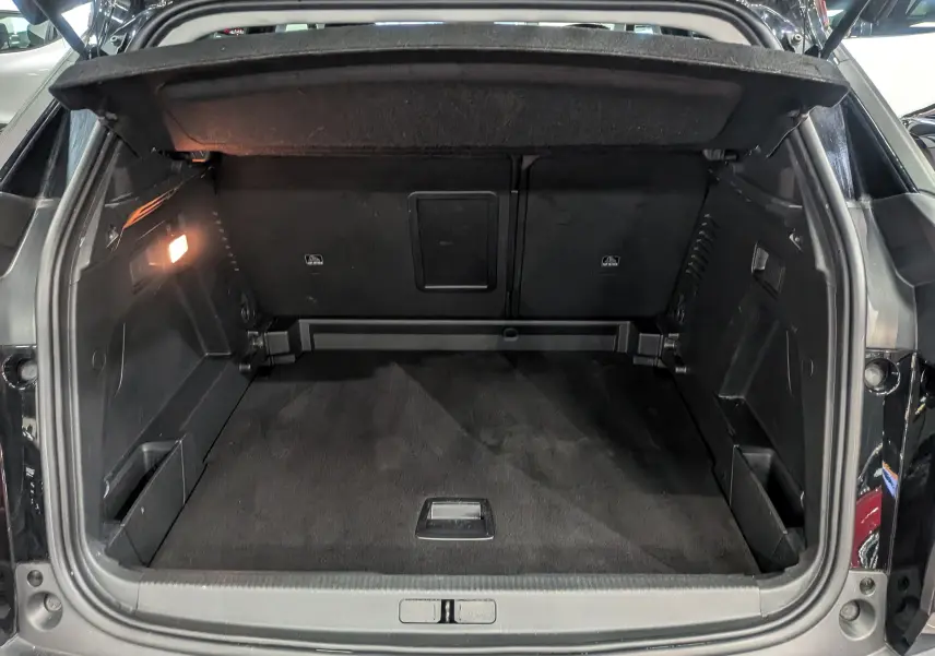 Coffre ouvert d'un Peugeot 3008 noir Perla, vue arrière montrant un espace de rangement propre et éclairé à gauche.
