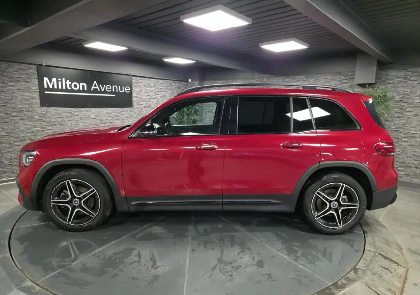 Vue latérale droite d'un Mercedes GLB rouge Patagonie avec jantes AMG 19 pouces et vitres teintées foncées.