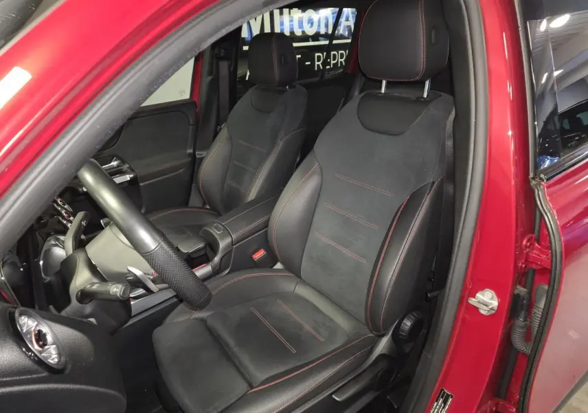Vue intérieure côté conducteur d'un Mercedes GLB rouge, sièges sport noirs avec surpiqûres rouges visibles.