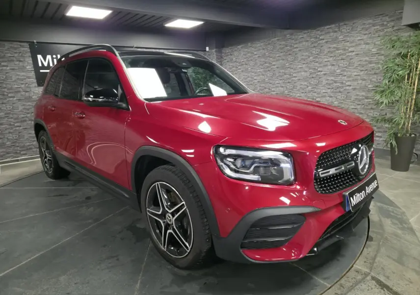 Mercedes GLB rouge Patagonie 3/4 avant droit avec jantes AMG noires et calandre noire brillante en intérieur showroom.