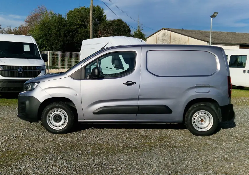 Vue de profil côté gauche d'un Peugeot Partner gris Artense utilitaire avec porte latérale pleine, stationné sur un sol gravillonné.