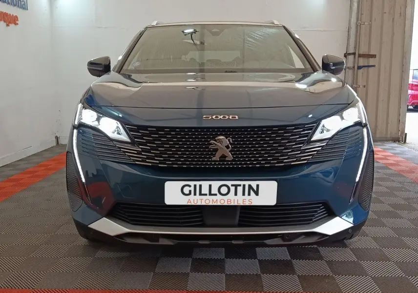 Vue avant d'un Peugeot 5008 bleu 2023 avec calandre noire et feux LED allumés en intérieur showroom.