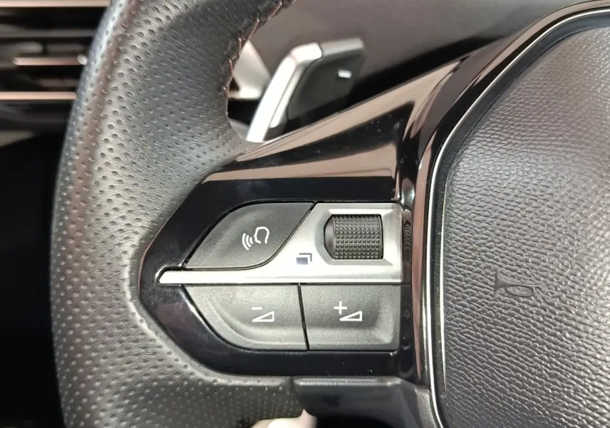 Gros plan sur les commandes gauche du volant cuir perforé du Peugeot 5008 GT 2023, boutons multifonctions noirs.