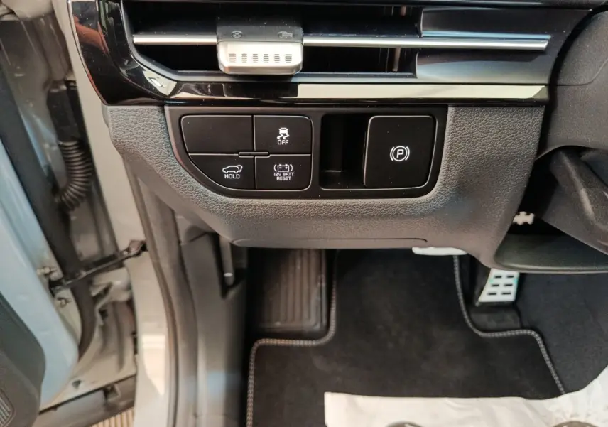 Détail des commandes sous le tableau de bord côté gauche du Kia Sportage gris foncé 2026, avec bouton frein à main électrique.