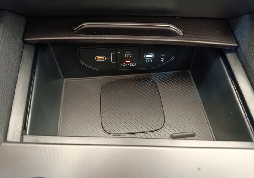 Vue rapprochée de la zone de recharge sans fil et ports USB du coffre central noir du Kia Sportage gris foncé 2026.