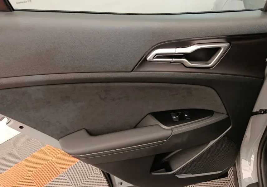 Vue intérieure côté gauche de la porte avant d’un KIA SPORTAGE gris foncé avec garniture noire et commandes de vitres.