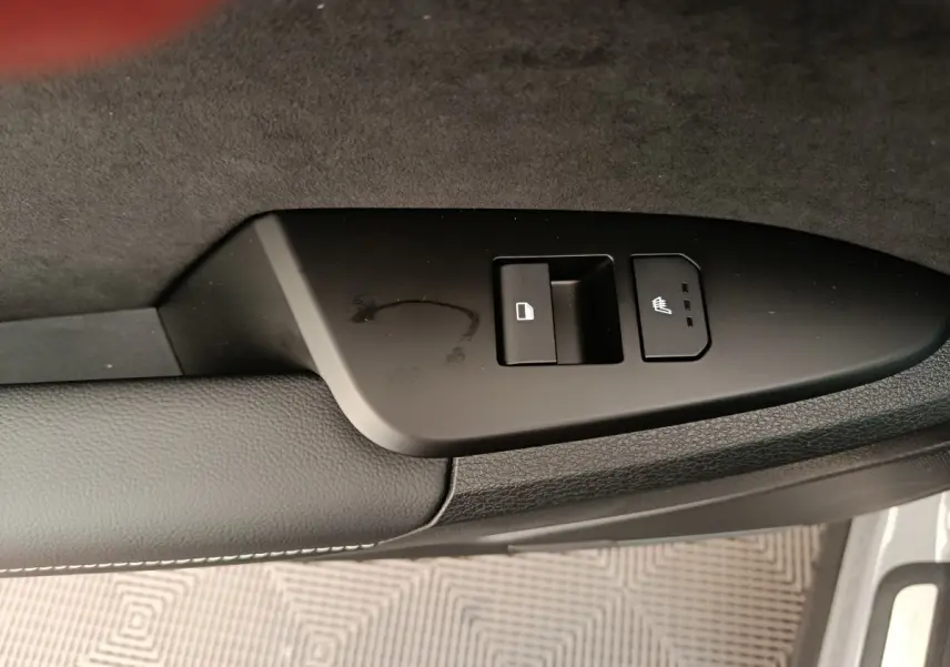 Gros plan sur la commande de verrouillage et siège chauffant côté porte avant d’un Kia Sportage gris foncé.