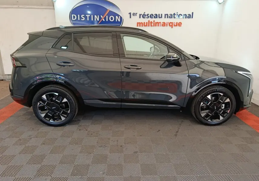 Vue latérale droite du KIA SPORTAGE gris foncé 2026 avec jantes noires et toit noir en showroom.
