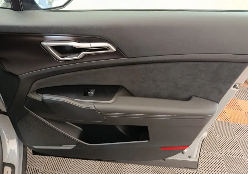 Vue intérieure côté gauche de la porte avant gris foncé du Kia Sportage avec poignée argentée et accoudoir rembourré.