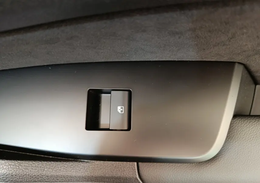 Bouton de commande de lève-vitre arrière droit sur panneau de porte intérieur noir d’un KIA Sportage gris foncé.