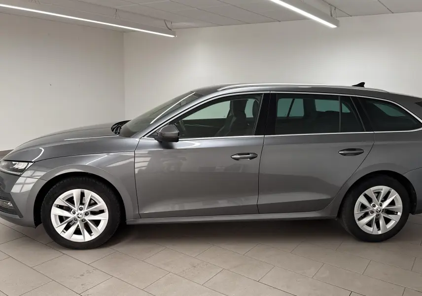 Skoda Octavia Combi 2023 gris graphite vue de profil côté gauche dans un intérieur neutre lumineux.