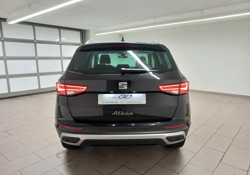 Vue arrière d'un SEAT Ateca noir Magic Nacré avec feux allumés et hayon électrique en intérieur showroom.