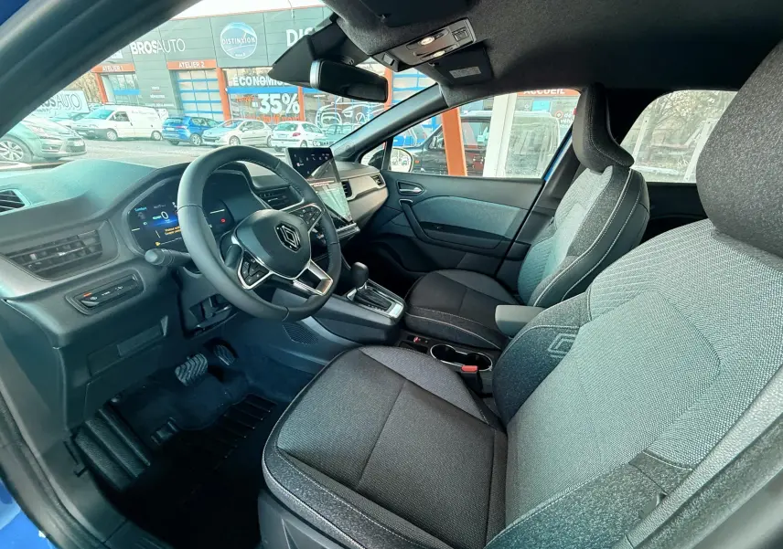 Vue intérieure côté conducteur du Renault Captur E-Tech Hybrid 2025, montrant sièges gris et tableau de bord moderne.