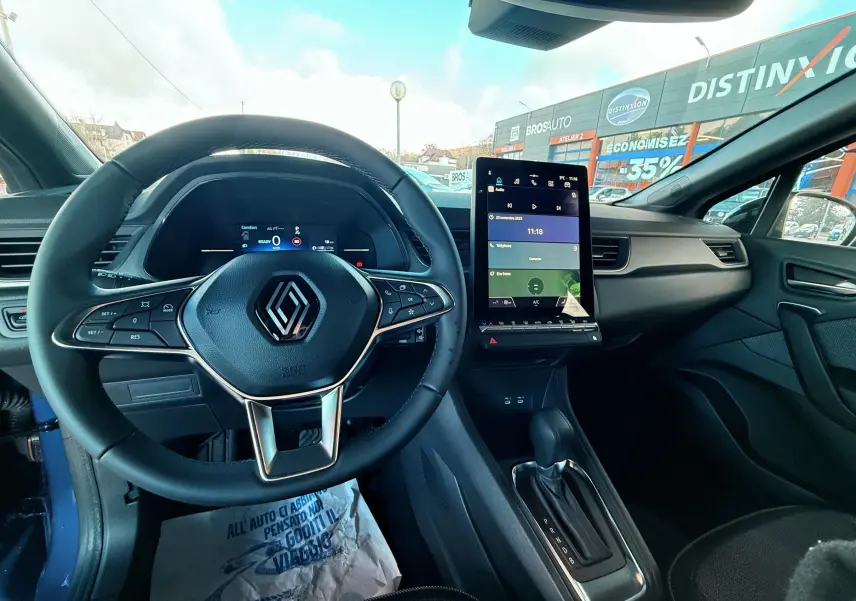 Vue intérieure avant du Renault Captur E-Tech Hybrid 2025, tableau de bord avec écran tactile vertical et volant multifonction noir.