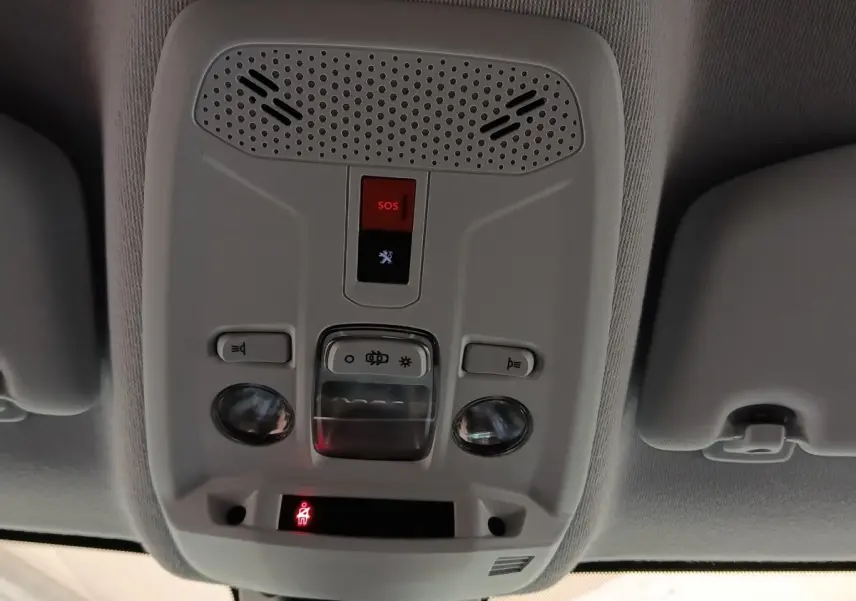 Vue en contre-plongée du panneau de commandes au plafond intérieur du Peugeot 208 blanc, avec bouton SOS rouge et éclairages intégrés.