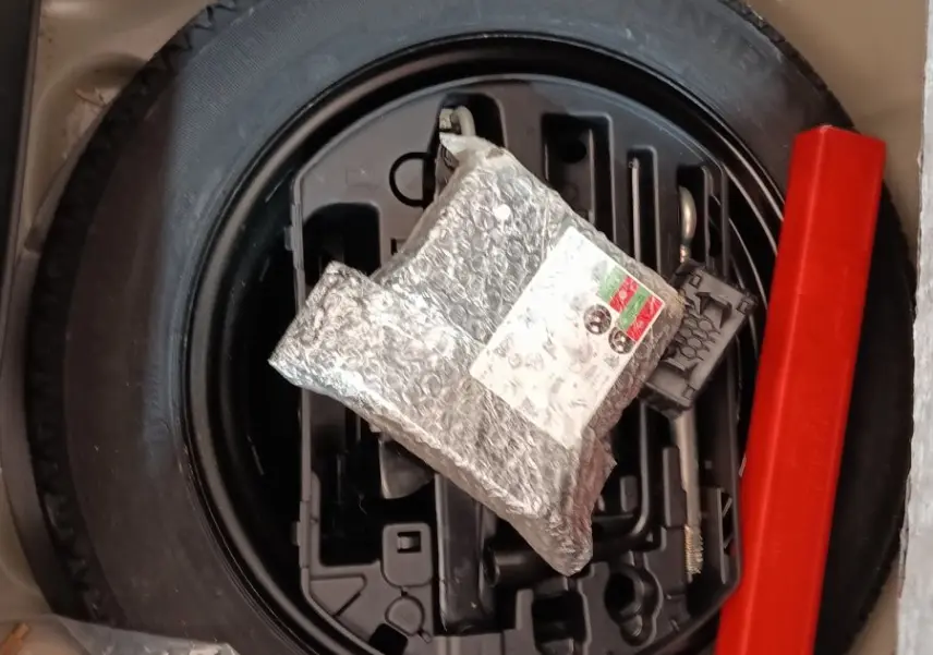 Vue plongeante sur la roue de secours noire et les outils de bord dans le coffre d’une Peugeot 208 blanche.