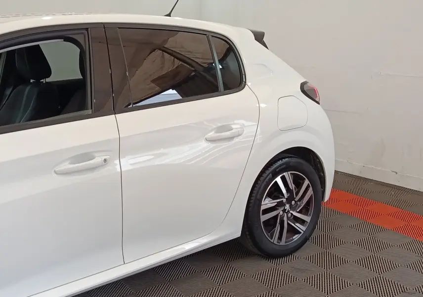 Vue latérale droite sur l’arrière d’une Peugeot 208 blanche avec jantes alliage et vitres teintées.