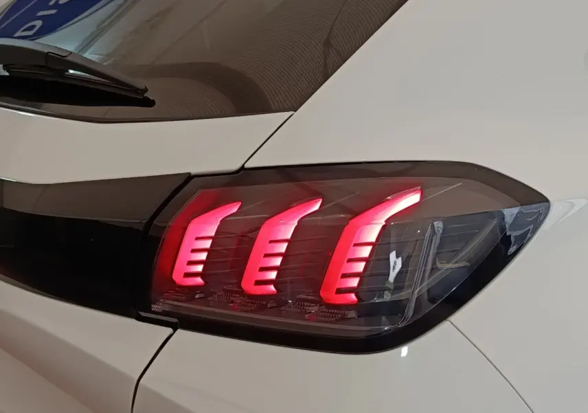 Gros plan sur le feu arrière droit allumé d'une Peugeot 208 blanche, soulignant son design à trois griffes LED.