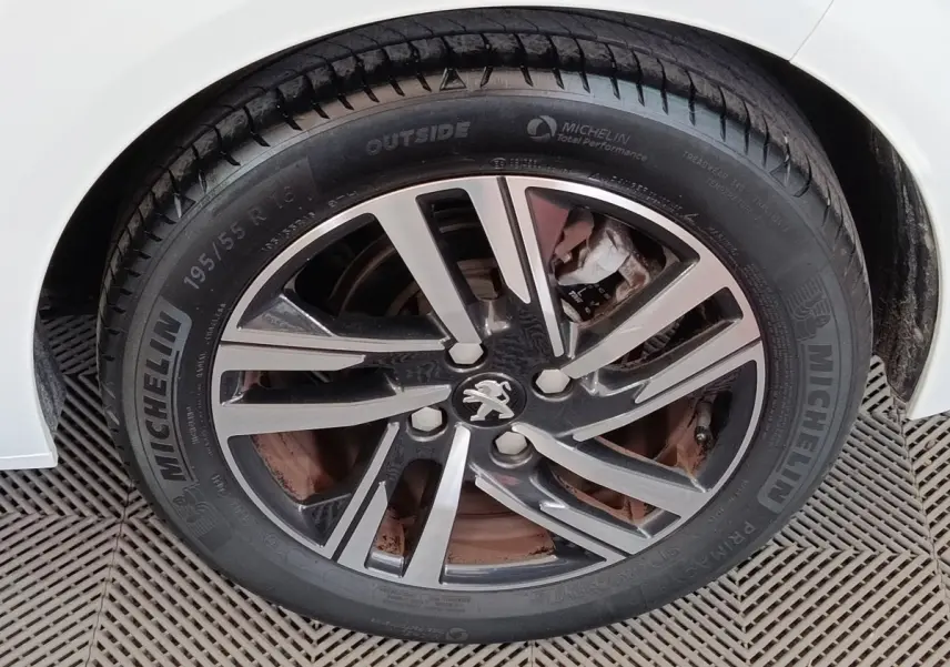 Gros plan sur la roue avant droite d'une Peugeot 208 blanche, avec jante alliage et pneu Michelin visible.