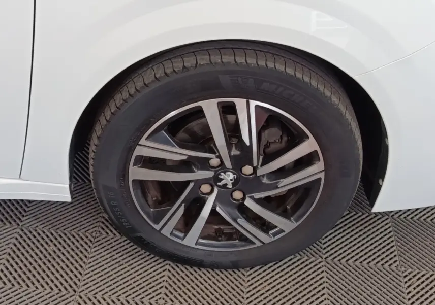 Gros plan sur la roue avant droite d'une Peugeot 208 blanche, avec jante alliage noire et argentée au design moderne.