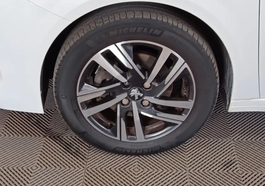 Gros plan sur la roue arrière droite d'une Peugeot 208 blanche avec jante alliage et logo lion au centre.