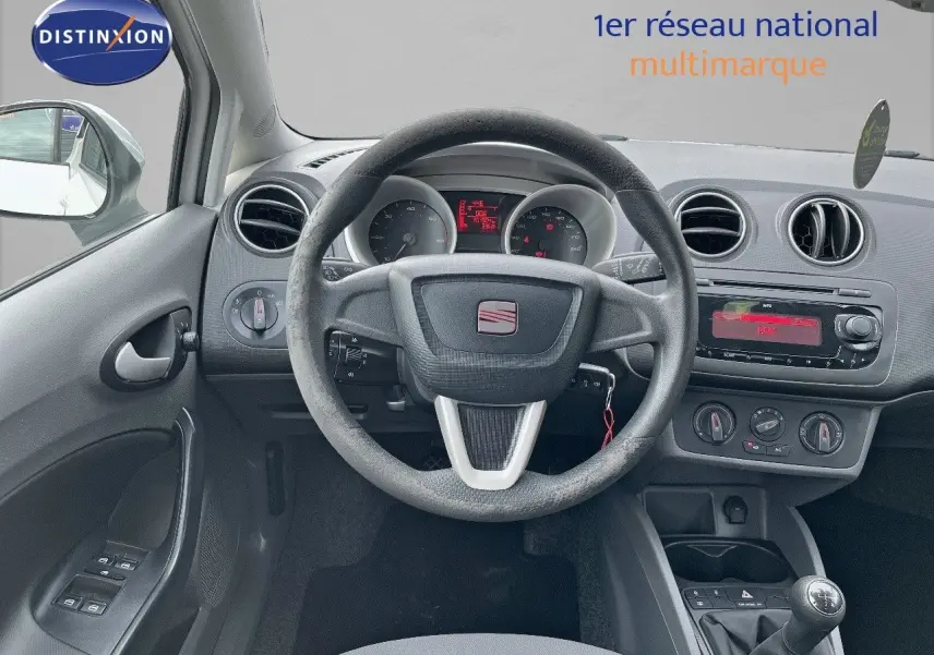 Vue intérieure centrée sur le volant et tableau de bord d'une SEAT Ibiza blanche 1.6 TDI 90CH STYLE de 2010 avec boîte manuelle.