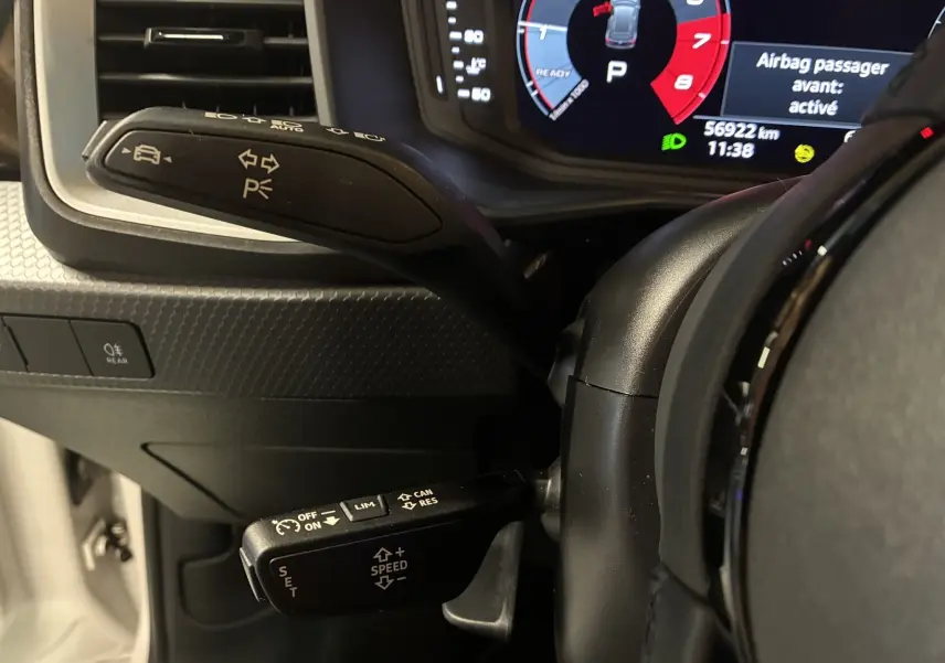 Gros plan sur les commandes au volant et le cockpit numérique de l'Audi A1 blanche, affichant 56 922 km.