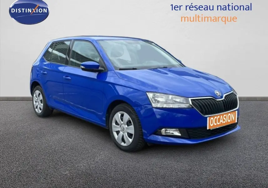 Vue avant d'une Skoda Fabia bleu énergie garée devant un garage avec enseigne AD Expert visible.