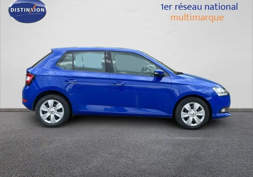 Vue 3/4 arrière droite d'une Skoda Fabia 2019 bleu énergie garée en ville, avec feux arrière allumés.
