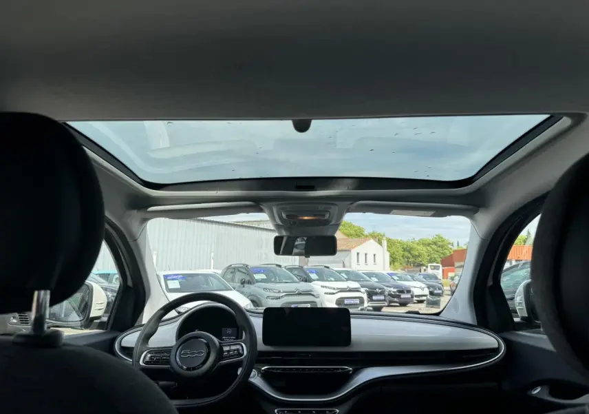 Vue intérieure avant de la Fiat 500 électrique blanche 2022, mettant en valeur le toit vitré panoramique et le tableau de bord épuré.