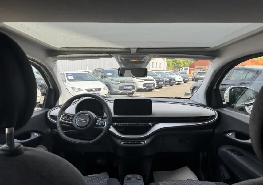 Intérieur de la Fiat 500 électrique 2022 vu de l'arrière, tableau de bord blanc avec toit panoramique et sellerie gris anthracite.