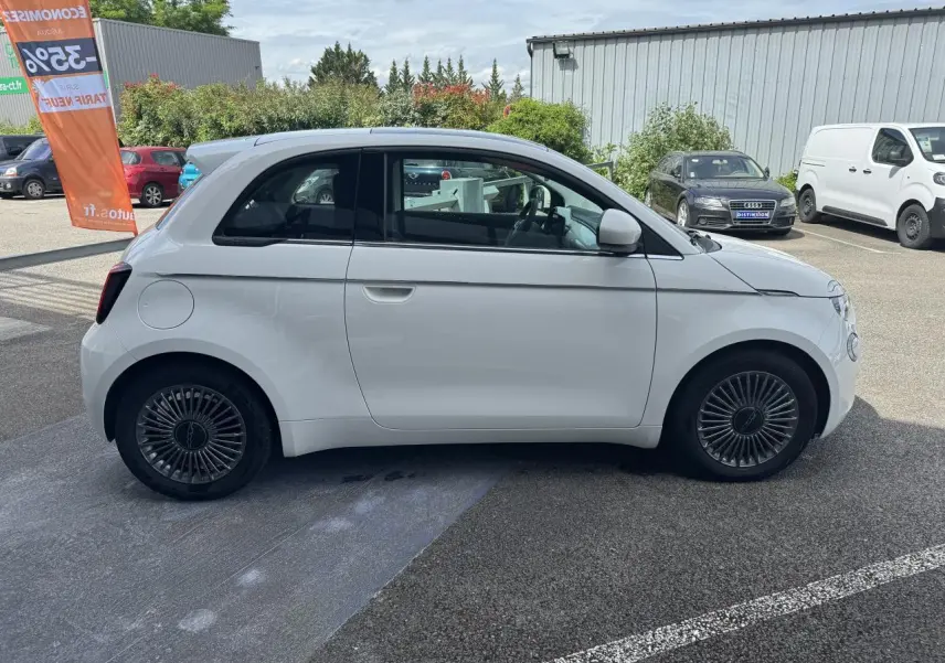 Profil droit d'une Fiat 500 électrique blanche 2022 avec jantes alliage 16'' Icône sur parking extérieur.