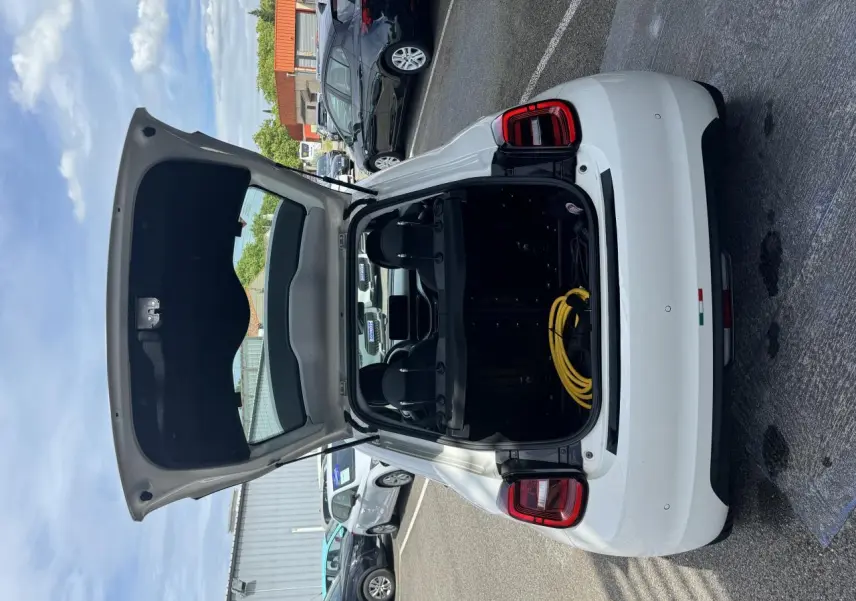 Vue arrière d'une Fiat 500 électrique blanche 2022 avec coffre ouvert et câble de recharge visible dans un parking.