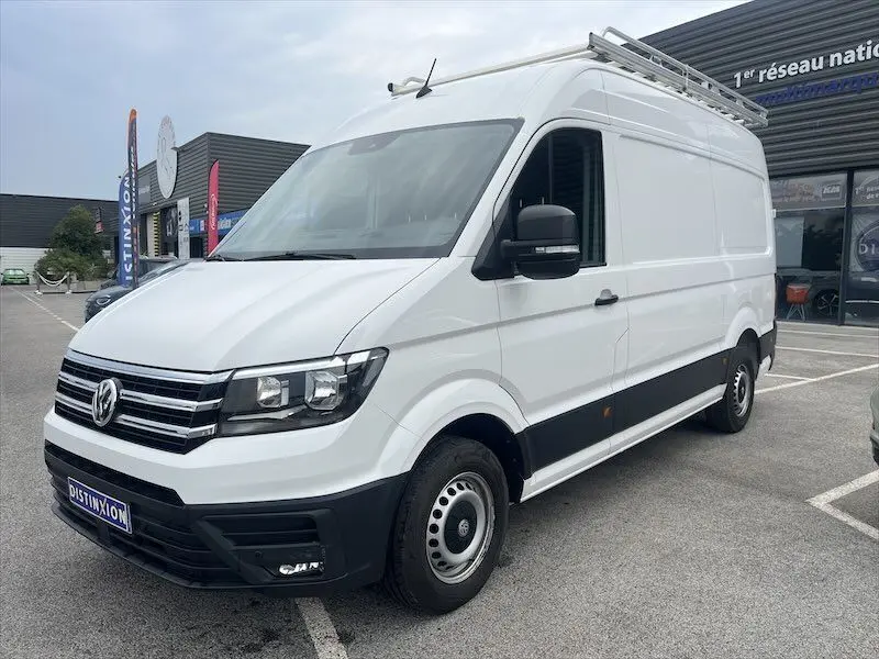 Fourgon Volkswagen Crafter blanc en 3/4 avant droit avec galerie de toit et jantes acier visibles sur parking.