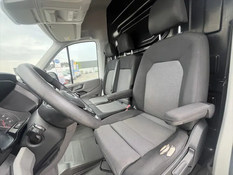 Vue intérieure côté conducteur du Volkswagen Crafter blanc, montrant les sièges avant gris avec accoudoirs et volant noir.