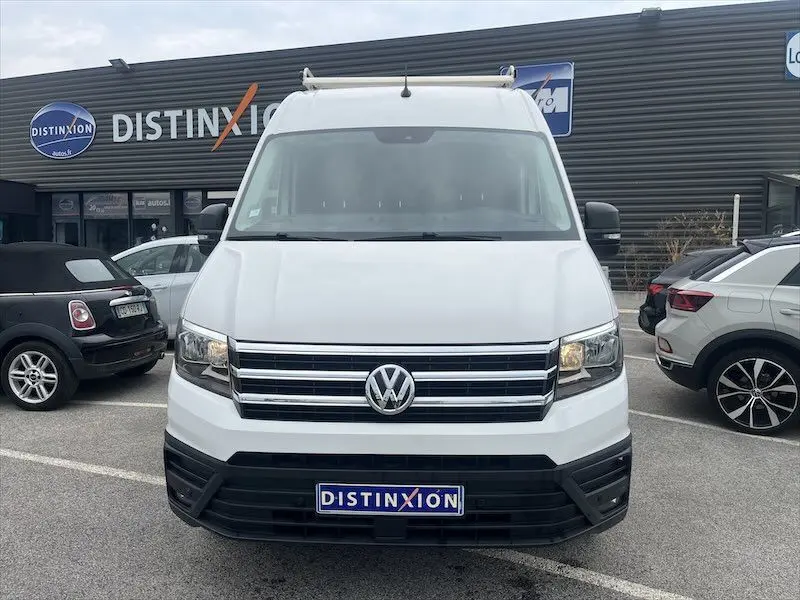 Vue de face d'un Volkswagen Crafter fourgon blanc avec galerie de toit, stationné devant un bâtiment Distinxion.