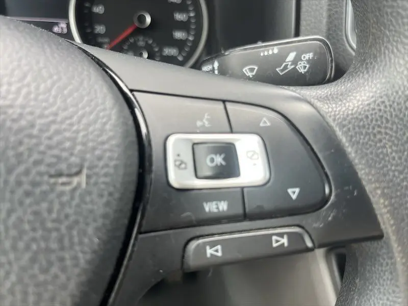 Gros plan sur les commandes au volant noir du Volkswagen Crafter Fourgon blanc, avec bouton OK et flèches directionnelles visibles.