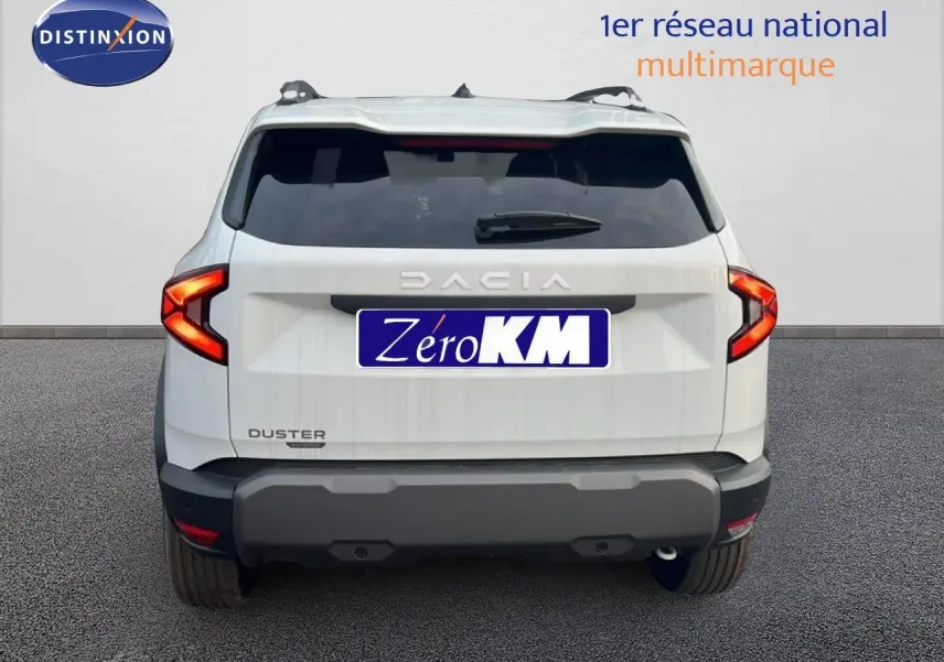 Vue arrière du Dacia Duster Hybrid 140 Journey blanc Glacier avec feux arrière en forme de C et barres de toit visibles.