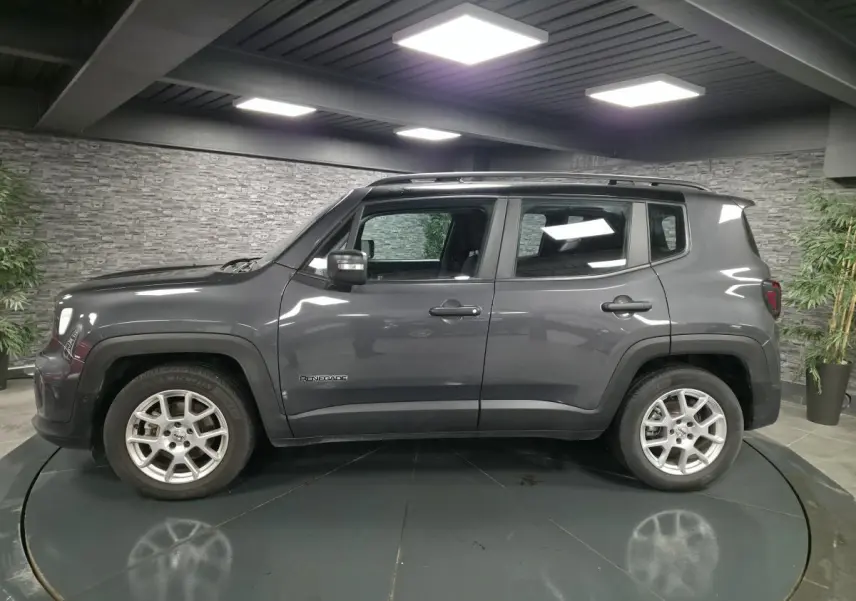 Jeep Renegade gris métallisé vu de profil côté gauche avec toit noir et jantes alliage 17 pouces en intérieur showroom.