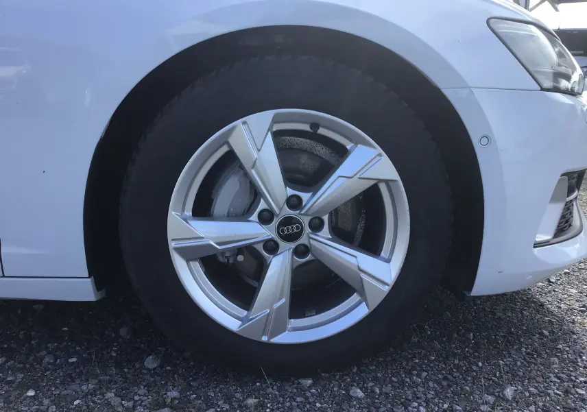 Gros plan sur la roue avant gauche avec jante argentée de l'Audi A6 Avant blanc glacier de 2022.