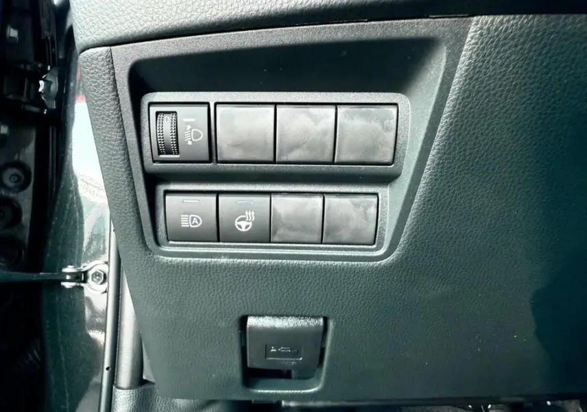 Gros plan sur les commandes de réglage des phares et du volant chauffant dans une Toyota Yaris Hybrid 2025 noire.