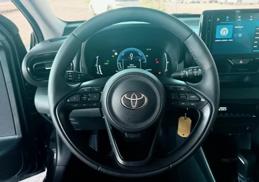 Vue rapprochée du volant noir de la Toyota Yaris Hybrid 2025 avec tableau de bord numérique et écran tactile central.