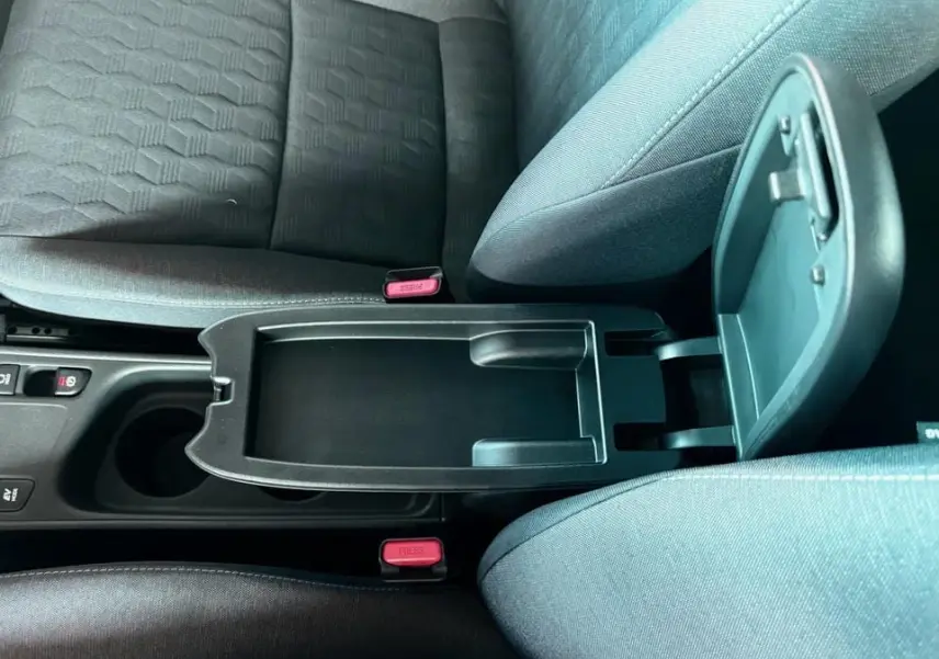 Vue rapprochée de la console centrale ouverte entre les sièges avant gris foncé d'une Toyota Yaris hybride 2025.