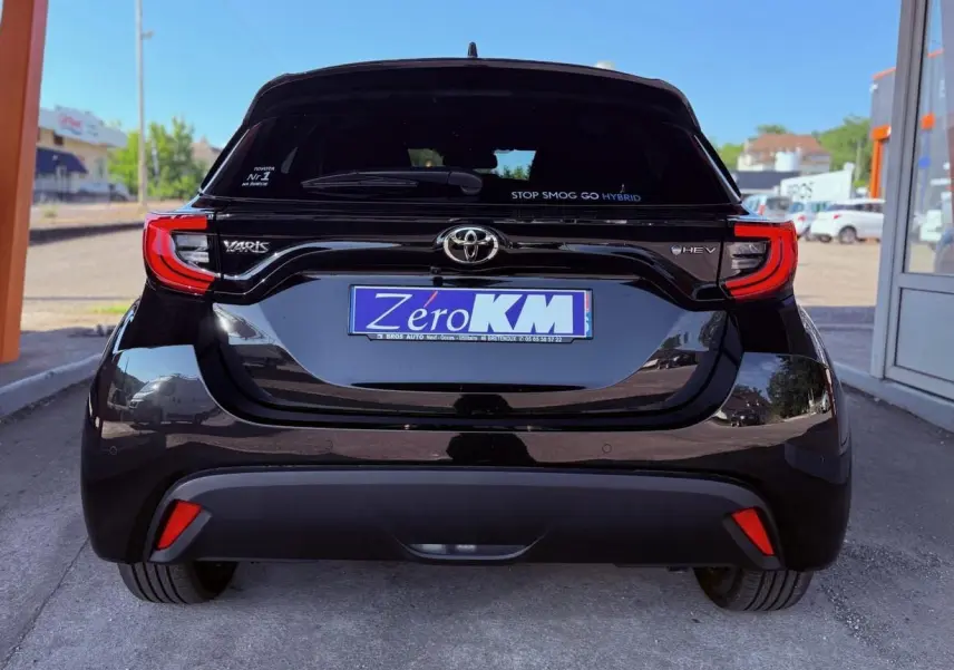 Vue arrière d'une Toyota Yaris Hybrid noire avec feux arrière LED et logo HEV sur un parking extérieur.