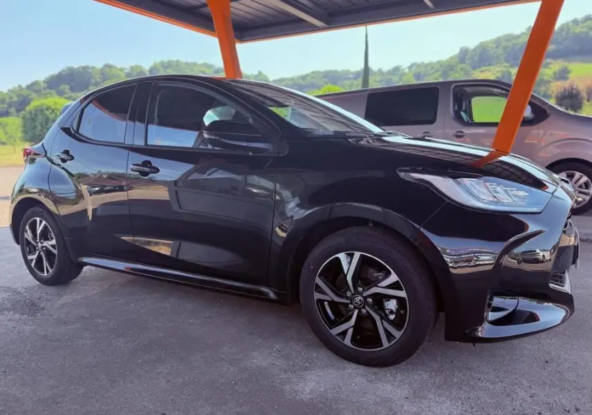 Toyota Yaris hybride noire vue de profil côté gauche sous abri avec jantes alliage et phares LED distinctifs.