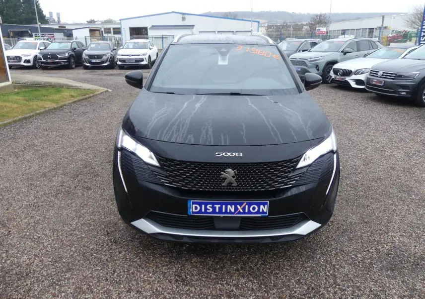 Vue frontale d'un Peugeot 5008 GT noir métallisé avec calandre chromée et feux LED allumés sur un parking.
