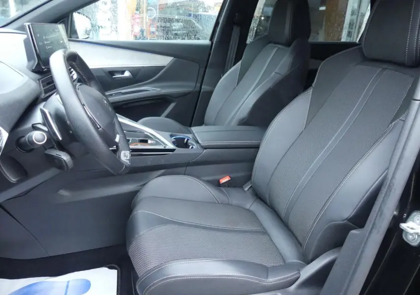 Vue intérieure côté conducteur du Peugeot 5008 GT 2023, sièges avant noirs en cuir et tissu avec surpiqûres contrastées.
